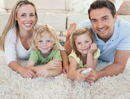 Family sitting in front of a couch smiling.